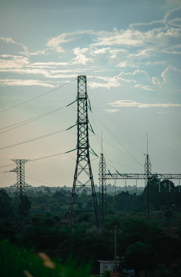 High-voltage power lines and towers in a rural setting under a cloudy sky.