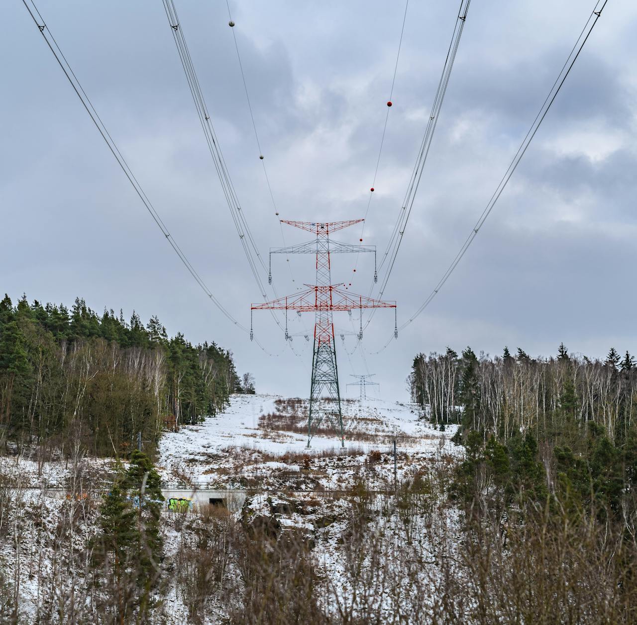 High-voltage power lines stretch through a wintry forest landscape, emphasizing energy and nature.