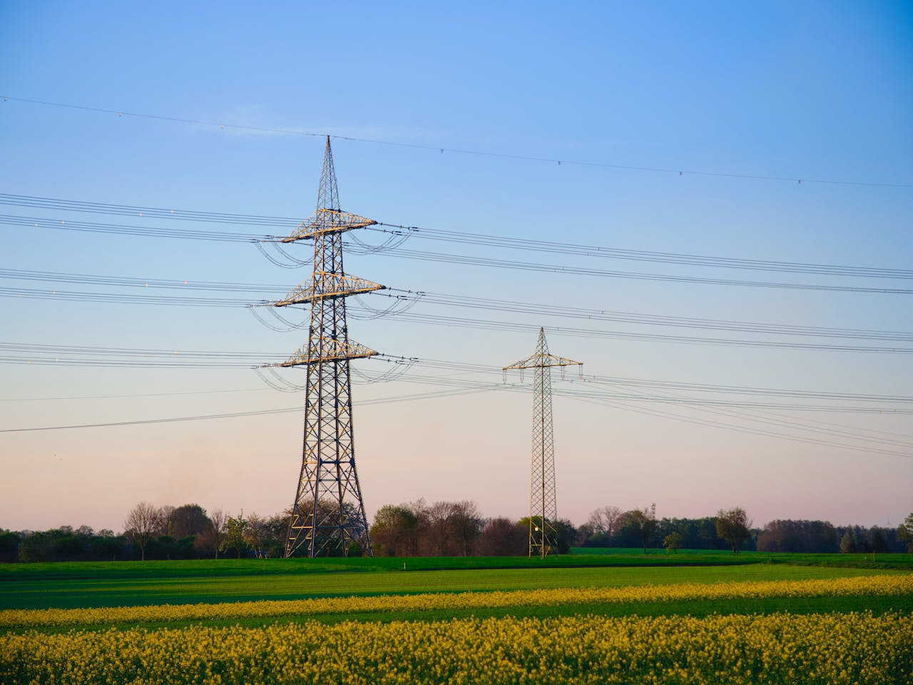Dusk landscape showing transmission towers and lush fields under a clear sky.