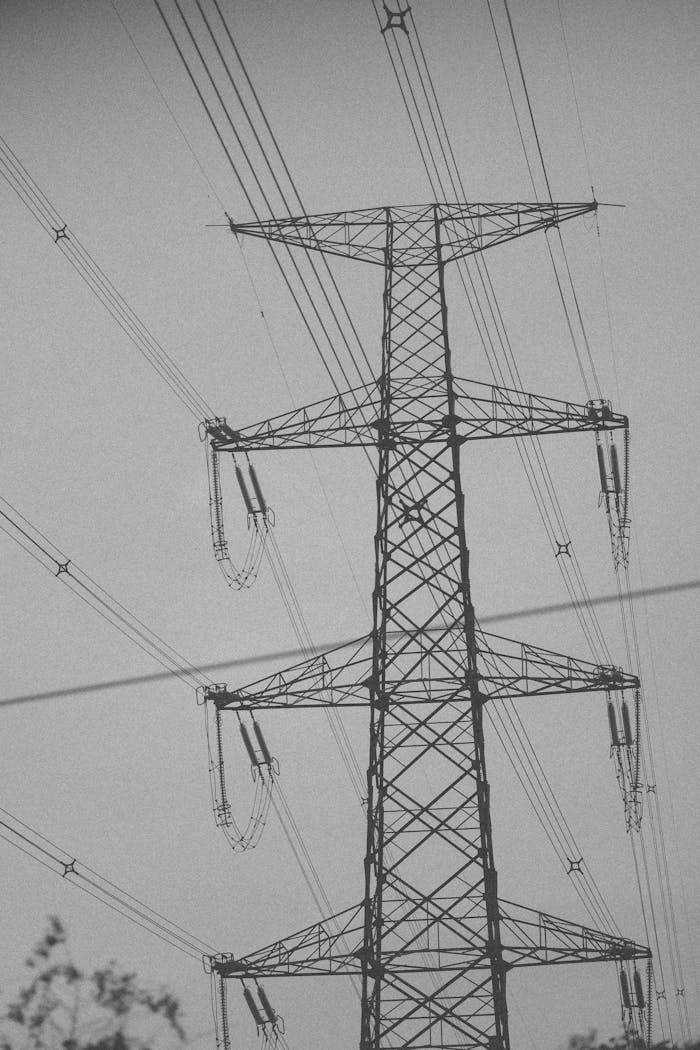 A towering steel pylon supporting multiple electric power lines in an industrial landscape.
